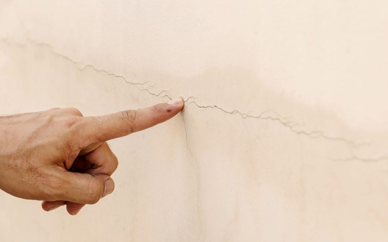 Close up of a man's hand pointing to a crack in the concrete wall.